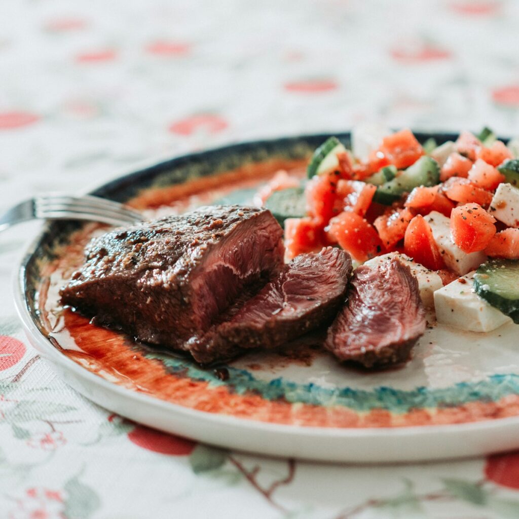 a plate of steak, carrots, and cucumbers