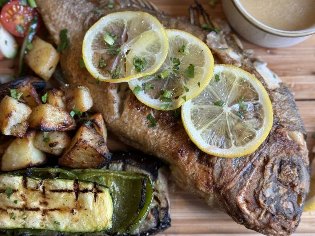 Whole roasted fish with lemon slices and grilled vegetables