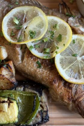 Whole roasted fish with lemon slices and grilled vegetables